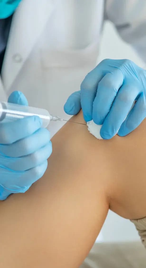 Gloved hands administering an injection into a patient’s knee.