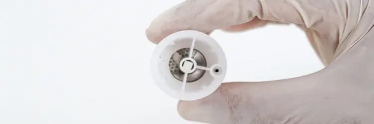 A gloved hand holding the round disaggregation grid of the single-use device.